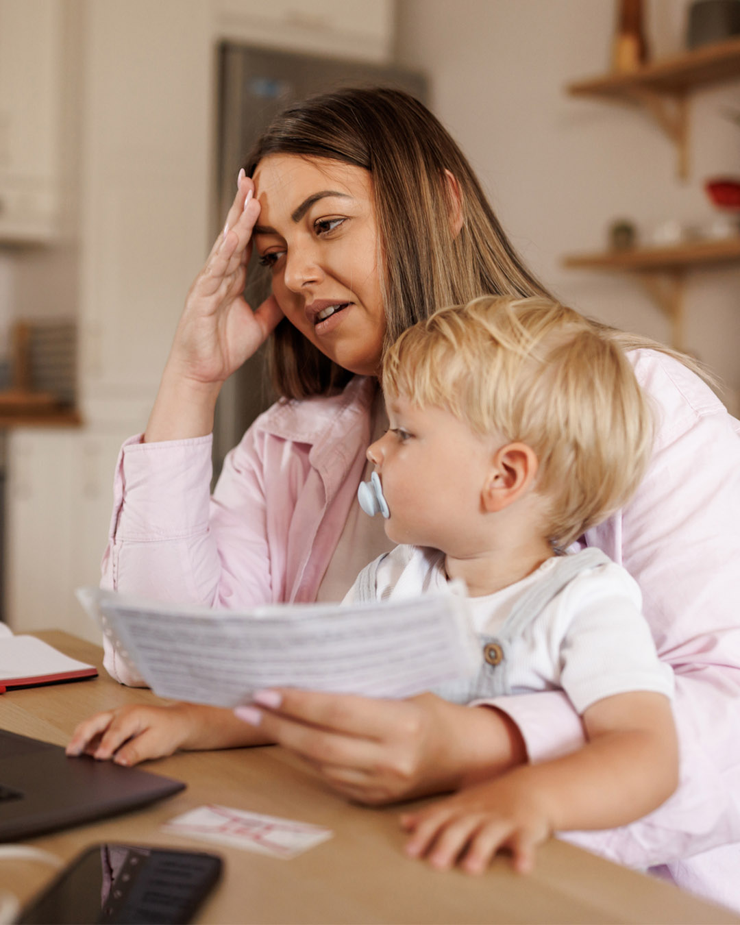 Worried single mother holding baby boy in her lap while paying bills at home stock photo